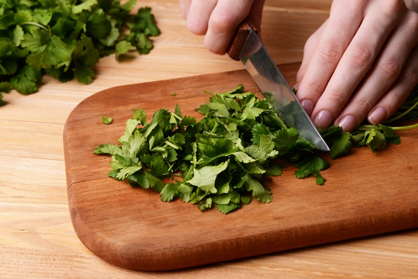 chopped cilantro on wooden board close up - Фасоль с шампиньонами в сметане
