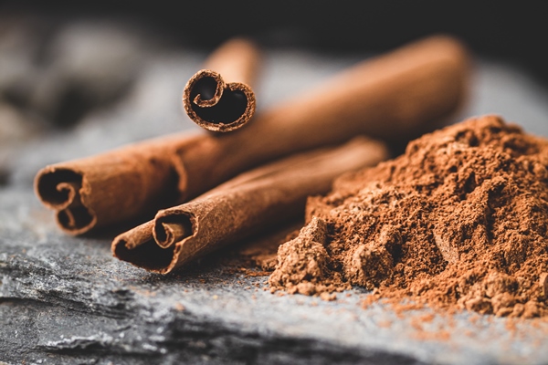 cinnamon stick and powder on black with stones - Оливковое масло с перцем и пряностями