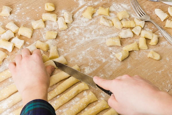 close up of a person cutting the dough with knife for preparing the homemade pasta gnocchi on wooden desk 1 - Шупфнудель (картофельные пальчики)