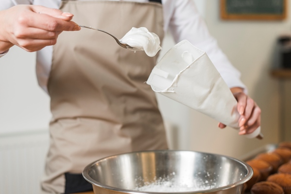 female baker filling whipped cream in the white icing bag - Морковный торт