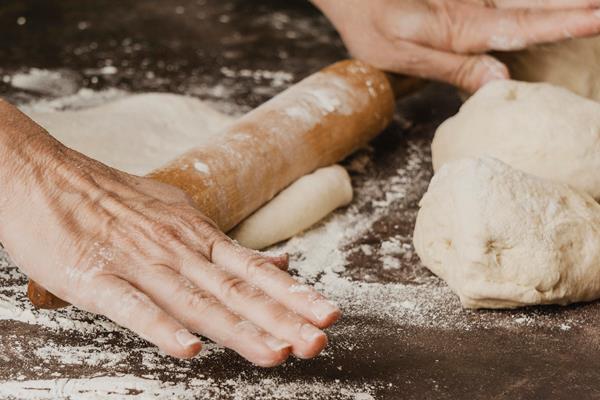 female chef rolling pizza dough on the table - Святочные кулинарные традиции: ржаной пирог с рыбой