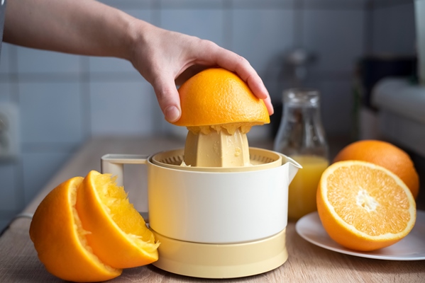 female hand squeezing orange juice from fresh oranges with a juicer in the home kitchen lose up - Кисель из апельсинов (школьное питание)