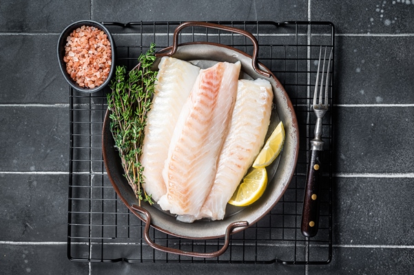 fresh raw cod fish fillets with herbs served on steel tray black background top view - Паровое суфле из пикши