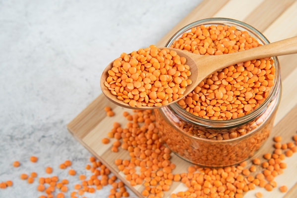 glass jar of red lentils with wooden spoon on wooden board - Чечевично-рисовые оладьи, постный стол