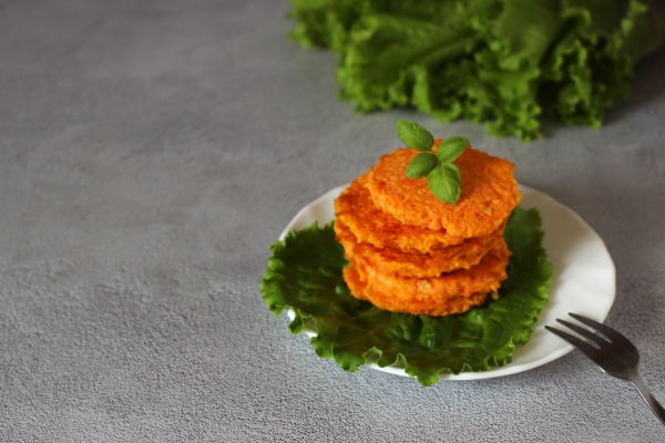 natural dietary carrot pancakes on a plate with lettuce leaves and a fork on a gray background - Пшённые оладьи с морковью и яблоками, постный стол