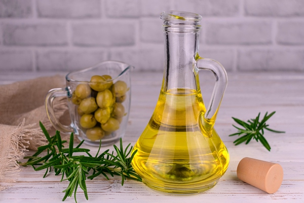 organic olive oil in a glass bottle and green olives with rosemary on a wooden background - Оливковое масло с перцем и пряностями