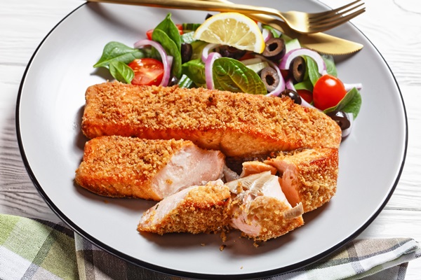panko crusted baked salmon fillets with spinach tomato cucumber olives salad on a plate on a white wooden table view from above - Камбала в панировке с сыром