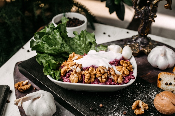 side view of beetroot salad with walnuts and sour cream on a wooden board - Салат из краснокочанной капусты с орехами