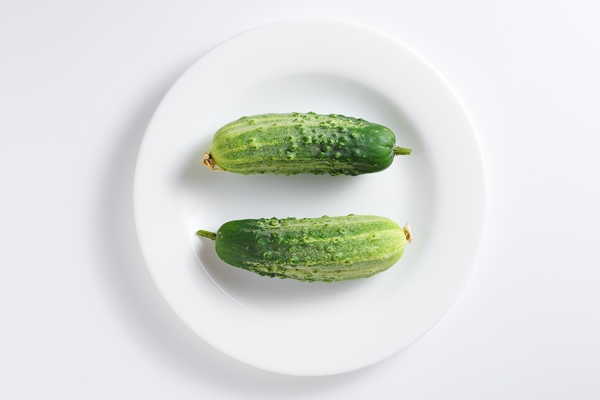 two fresh green cucumbers on a plate on white background top view - Салат с лососем и овощами