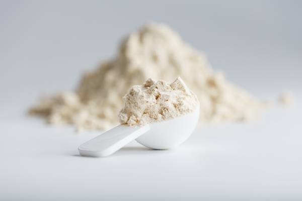 a pile of protein powder with a measuring spoon on a white background - Кекс с кэробом в кружке
