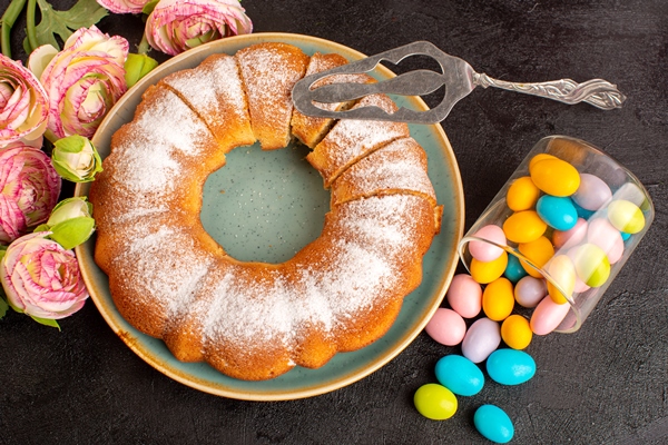 a top view sweet round cake with sugar powder along with colorful candies sliced sweet delicious isolated cake inside plate and grey background biscuit sugar cookie - Сахарная бабка