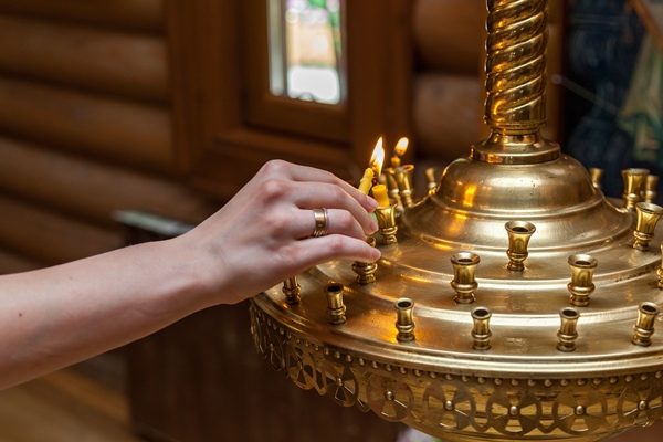 a woman in the church lights a candle - Кулинарные традиции празднования именин