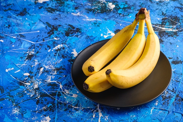 banana fruits in black plate on blue textured surface - Ржаные банановые маффины с кэробом