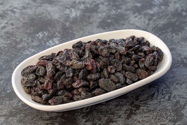 black raisins on plate on dark background - Оладьи с изюмом, постный стол