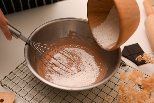 closeup female preparing a cookies dough adding a cup of flour into a mixing bowl in the kitchen - Постный кекс с вишней и кэробом