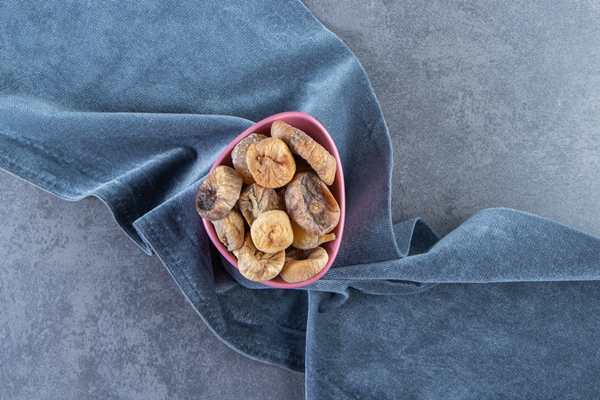 dried figs in a bowl on a piece of fabric on the marble background - Овсяная каша с кэробом, инжиром и бананом
