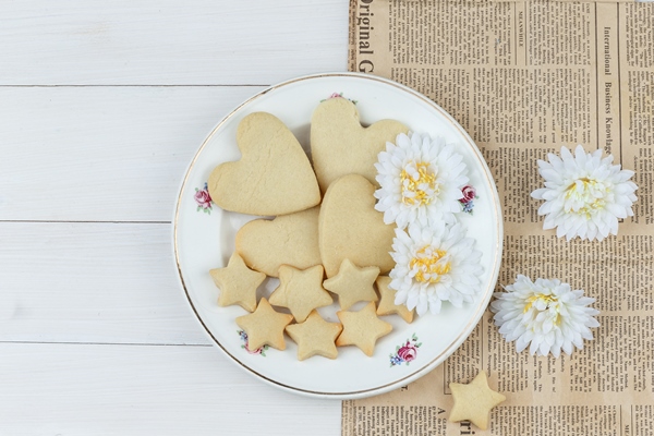flat lay cookies plate with flowers wooden newspaper background horizontal - Медовые пряники на молоке