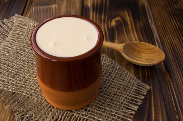 homemade ryazhenka in the brown ceramic jar on the rustic wooden background fermented milk product - Бутеня