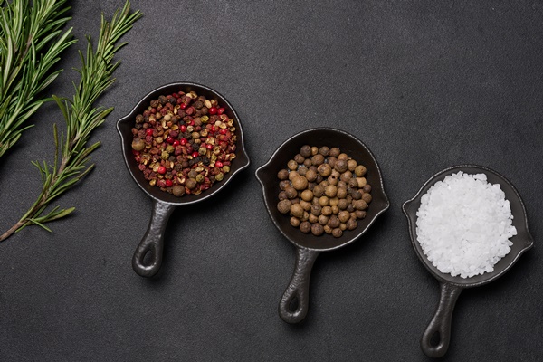 miniature pans with spices salt black pepper and fragrant pepper a sprig of rosemary on a black table spices for cooking - Бигос в мультиварке