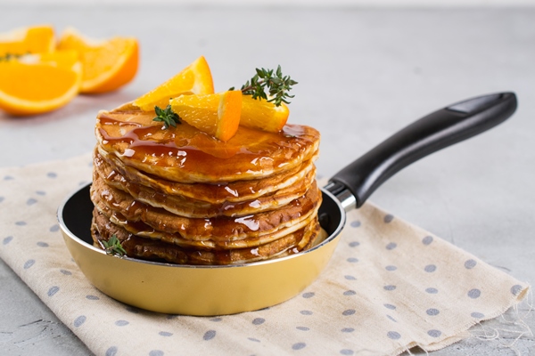 pancakes with orange and sprinkled maple syrup in a small yellow pan on white surface breakfast - Апельсиновые оладьи, постный стол