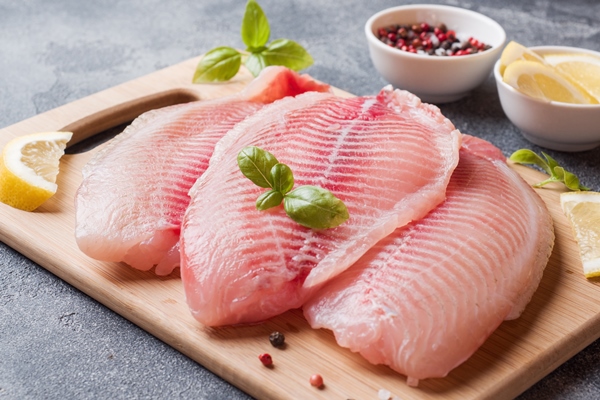 raw fish fillet of tilapia on a cutting board with lemon and spices dark table - Рыба в кляре