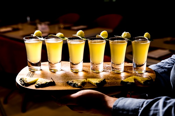 side view of set of alcoholic cocktails in shot glasses with pineapple slices on wooden board on dark background 1 - Банкет