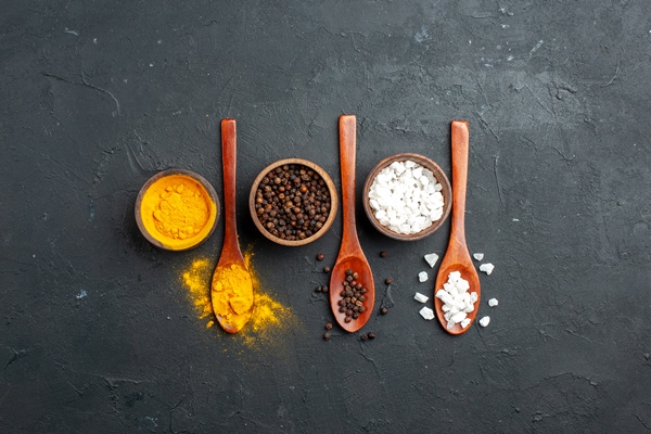 top view bowls with turmeric black pepper sae salt wooden spoons on black surface with copy place - Кугель овощной в мультиварке