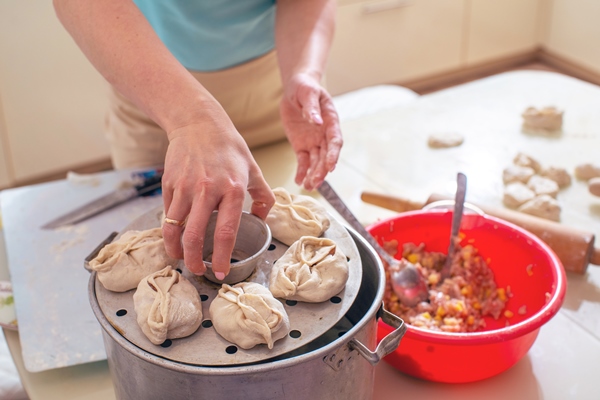 uzbek national food manta like dumplings on a special steamer a woman holding in her hand horizontal frame - Манты с рыбой и тыквой