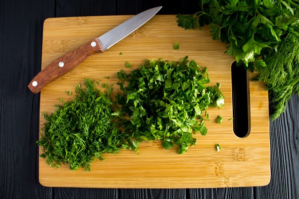 chopped parsley dill cutting board black wooden table top view - Салат из капусты с уксусом и растительным маслом