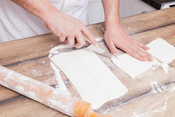 close up man s hand cutting rolled dough with knife table - Булочки из слоёного теста