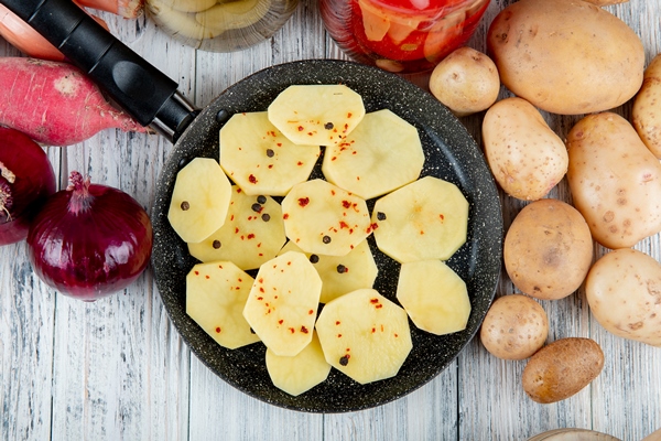 close up view potato slices with black pepper pan onion radish potatoes around wooden background - Картофель, жаренный кружочками