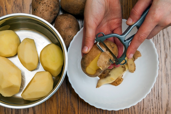 detail woman hands peeling fresh yellow potato with kitchen peeler food preparation concept - Постные драники с яблоками