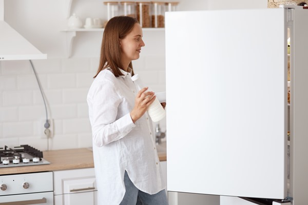 profile portrait attractive dark haired woman wearing white shirt looking smiling inside fridge with positive emotions holding plate hands posing with kitchen set background - Секреты хозяйки: как снять сливки с молока