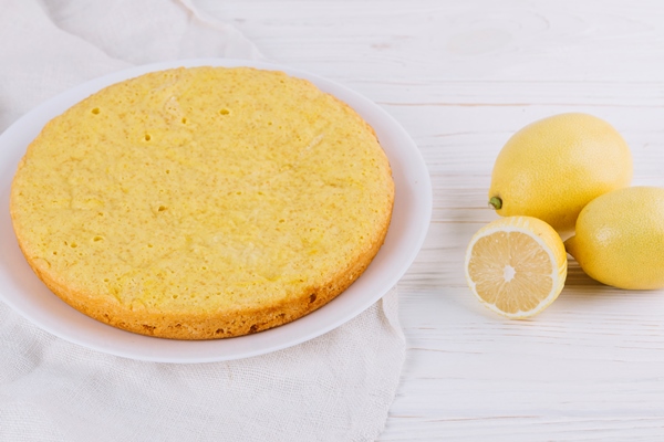 round lemon cake served white plate with whole lemons wooden backdrop - Постный лимонный пирог