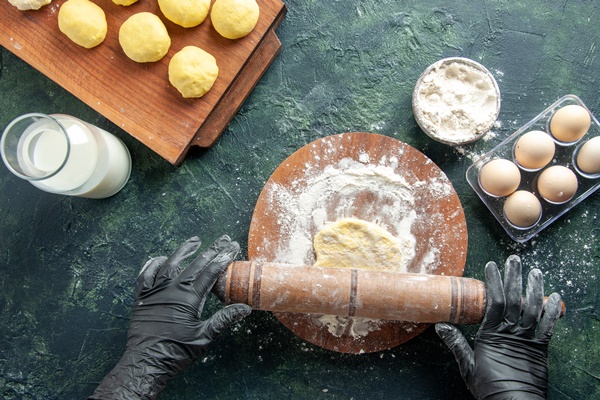 top view female cook rolling out dough with flour dark surface - Пончики бездрожжевые