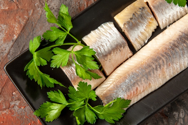 top view fresh sliced fish with greens lemon pieces inside black pan dark background - Начинка для блинчиков из сельди