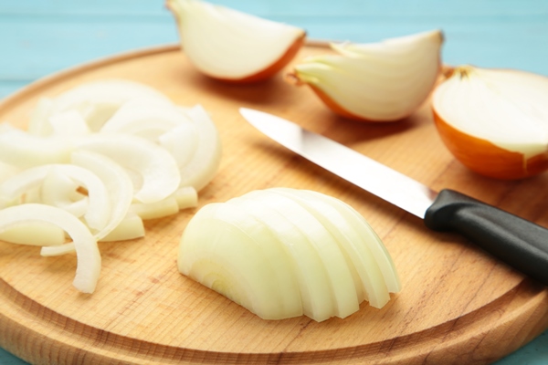 whole sliced yellow onions wooden cutting board top view - Блинчики с картофелем