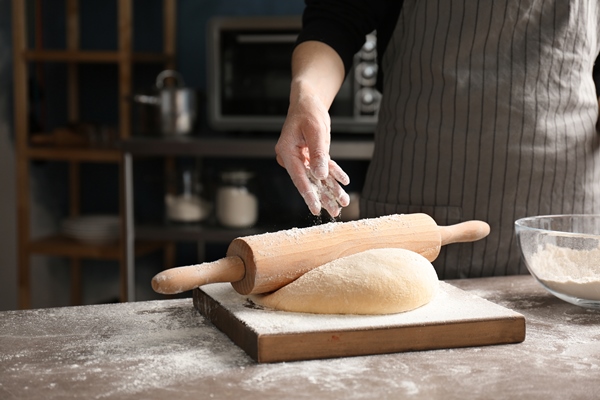 woman sprinkling flour dough table kitchen - Булочки с корицей