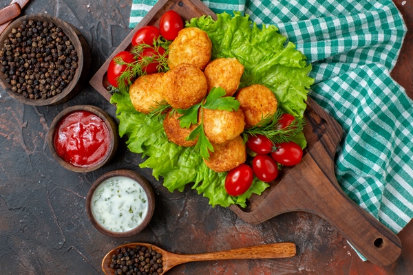 top view chicken nuggets lettuce cherry tomatoes wood board black pepper bowl sauces small wooden bowls wooden spoon dark surface - Картофельные котлеты с грецкими орехами